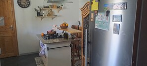 Eine kleine Küche mit eingebautem Gaskochfeld, Holzregalen, einer Obstschale und einem Kühlschrank mit Magneten und Notizen.