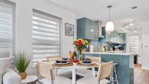 Una cocina moderna con una isla central, sillas blancas para comer y una mesa de comedor preparada para cuatro.