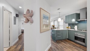 Una cocina moderna con una isla central, un comedor y un pasillo que conduce a un dormitorio.