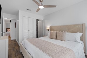 Ein Schlafzimmer mit Bett, Deckenventilator, Nachttisch, Lampe und Kleiderschrank.