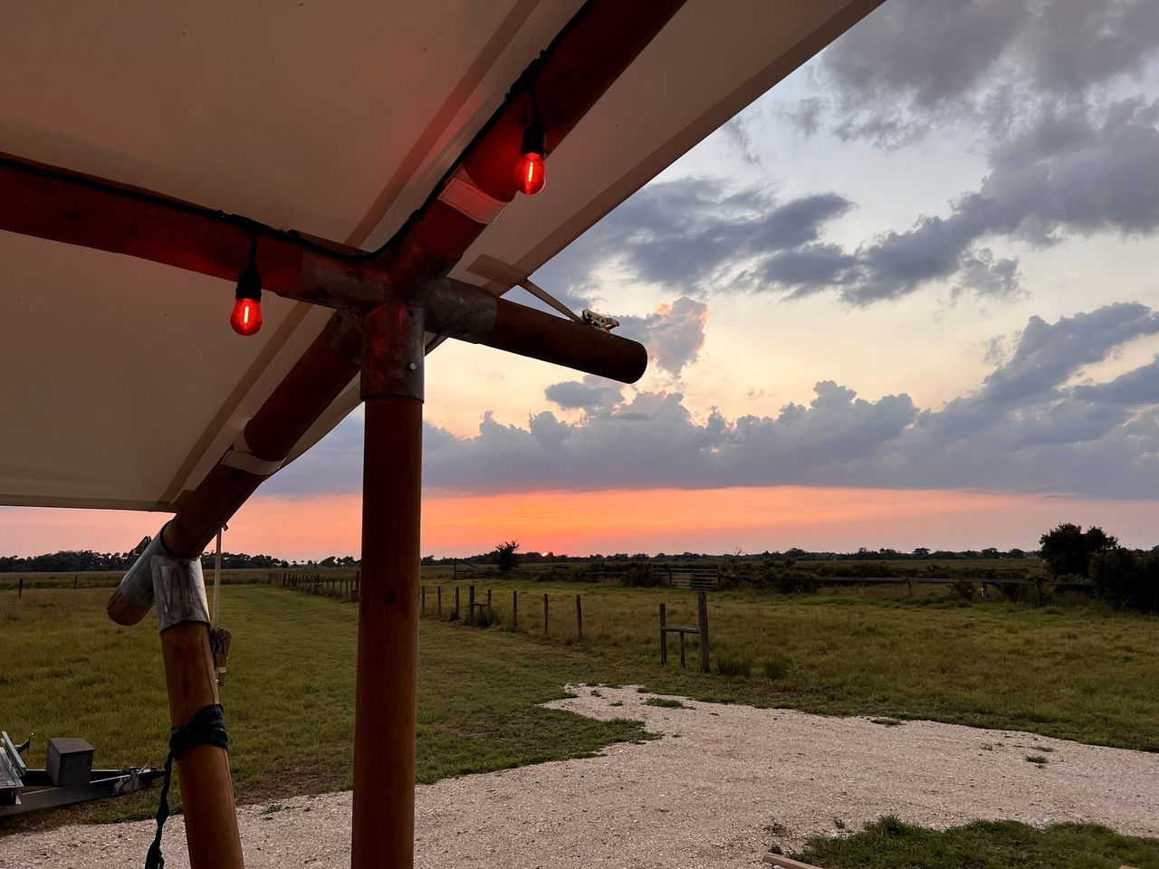 A rural landscape with a gravel path, wooden fence, and a sunset view.