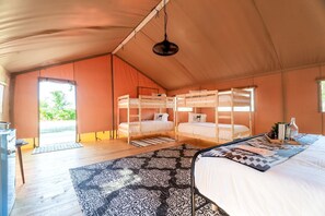 Un alloggio in tenda con letti a castello, una lampada a sospensione e vista sul verde circostante.