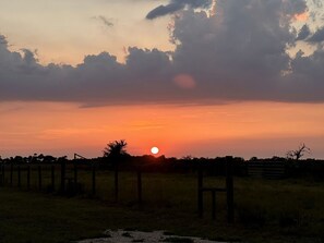 Tramonto su un paesaggio rurale con una recinzione e alberi.