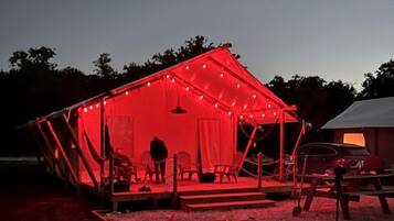 A tent with a fire pit and seating area, surrounded by trees.