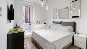 Un dormitori modern amb un llit gran, una taula de nit, un mirall, un tocador amb un rentapins i una finestra amb cortines.