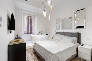 Ein modernes Schlafzimmer mit einem großen Bett, einem Nachttisch, einem Spiegel, einem Schminktisch mit Waschbecken und einem Fenster mit Vorhängen.