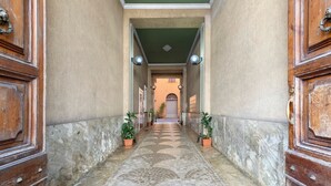 Passadís amb sòl de rajola, amb portes de fusta i nanses metàl·liques a ambdós costats, que condueix a una habitació amb sostre verd i una porta amb finestre.