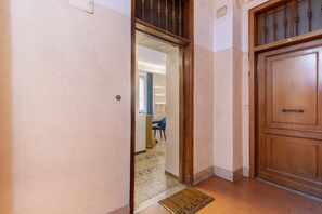 A hallway with a wooden door, a doormat, and a glimpse of a room with a blue chair and a table. - Ellie Luxury Apartment with Balcony, Wi-Fi, and Air Conditioning (Rome)