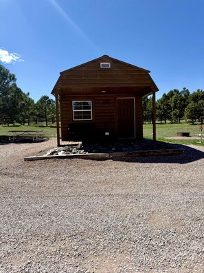 A wooden cabin with a porch, a door, and a window. - Group 34) Cabin - King Bed (Rapid City)