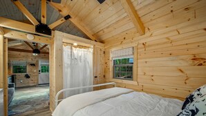 Une chambre à coucher située dans une cabane en bois, avec un lit, une fenêtre, une porte et une vue sur l’extérieur.