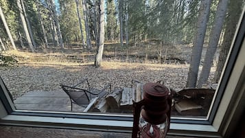 A window with a view of a forested area, a metal chair, and a red lantern on the windowsill.