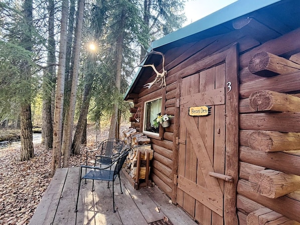 A rustic cabin with a wooden exterior, a porch with chairs, and a sign reading 'Beast Den.'