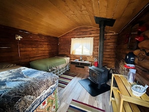 A cozy cabin with a bed, a small table, a stove, and a window.