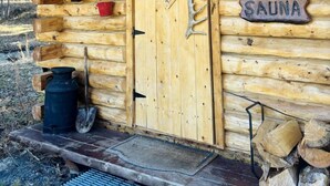 Une cabane en bois avec une porte, une pancarte de bienvenue, un seau et une pelle à l’extérieur.