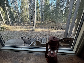 A window with a view of a forested area, a metal chair, and a red lantern on the windowsill.