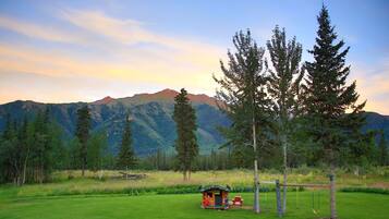 A grassy field with a small wooden structure, trees, and mountains in the background.