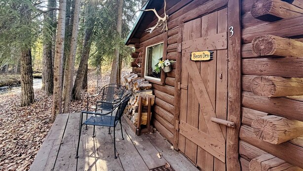 Une cabane rustique aux murs en bois, avec une véranda dotée de chaises et une pancarte sur laquelle on peut lire : « Repaire de la Bête ».