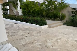 Una terrazza in cemento con gradini che conducono a un muro bianco, circondata da vegetazione e una scala.