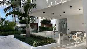 Un espacio exterior moderno con zona de estar, palmeras y un edificio con amplios ventanales.