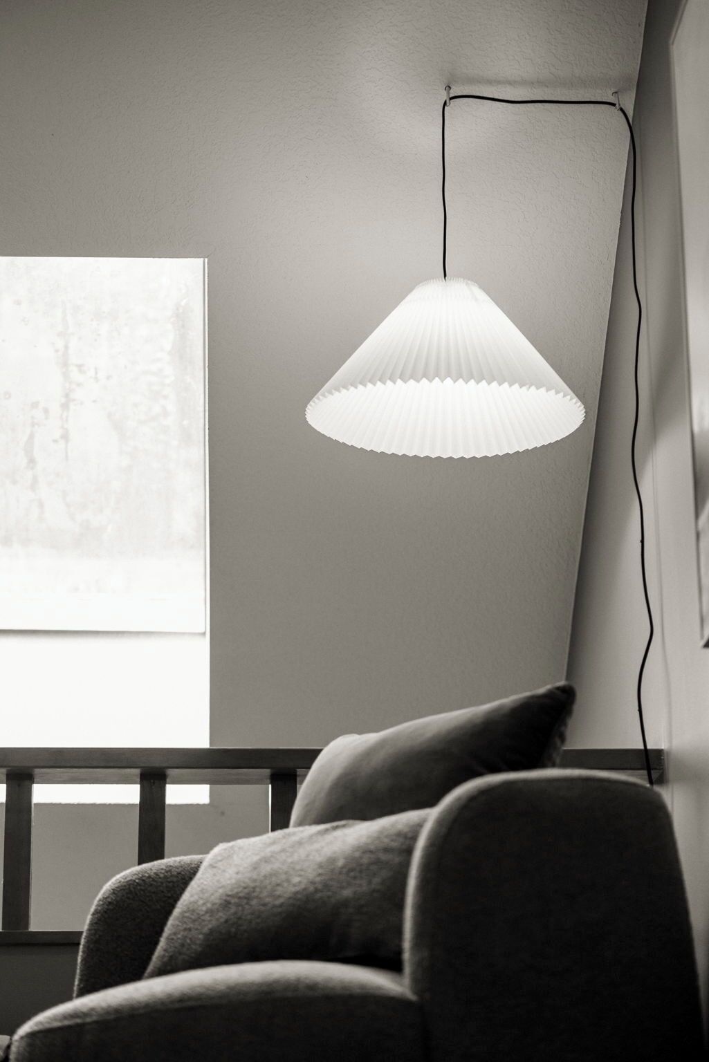 A room with a white paper cone pendant light, a gray sofa, and a large window with a view.