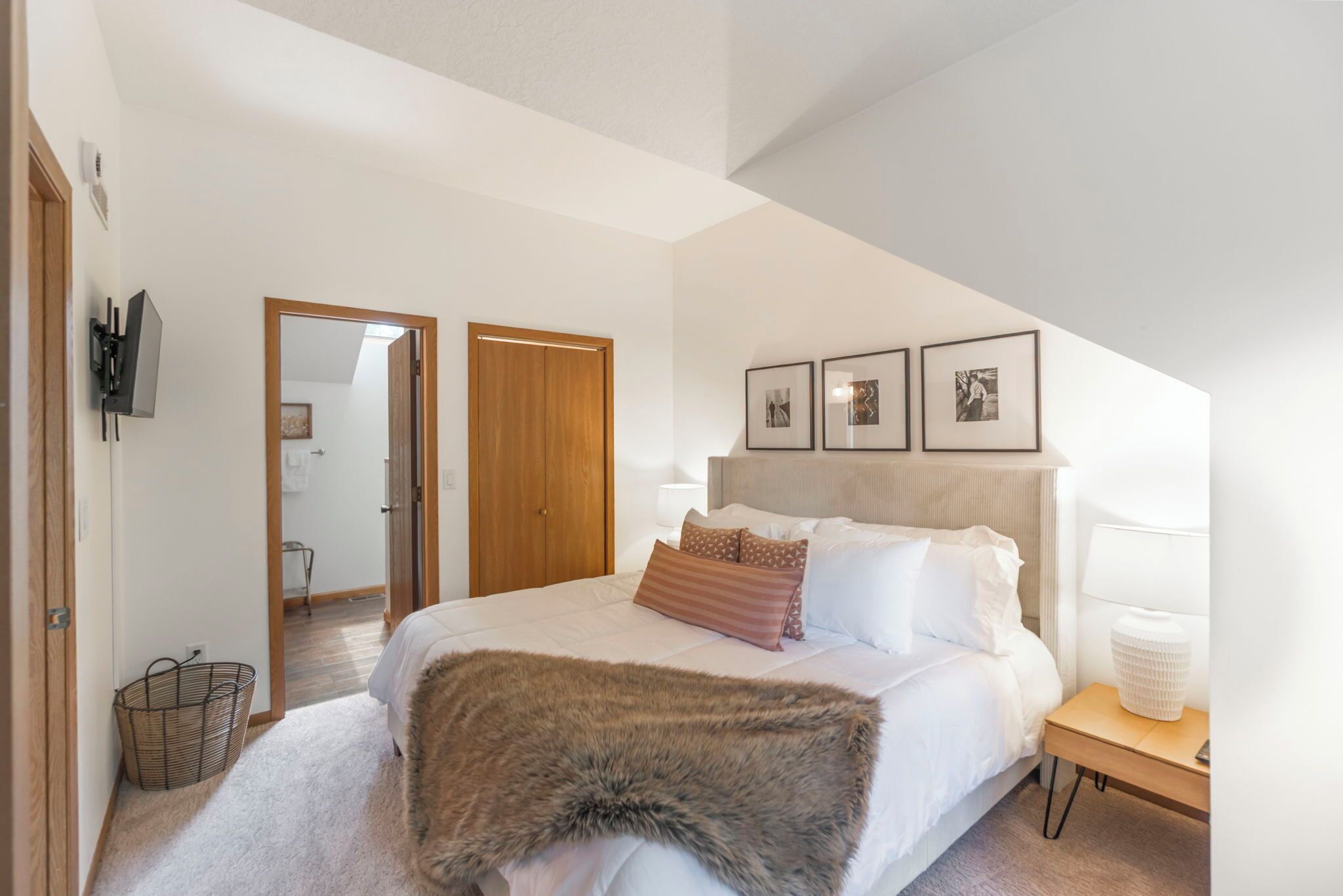 Ein Schlafzimmer mit Bett, Nachttisch, Lampe und gerahmten Bildern an der Wand.