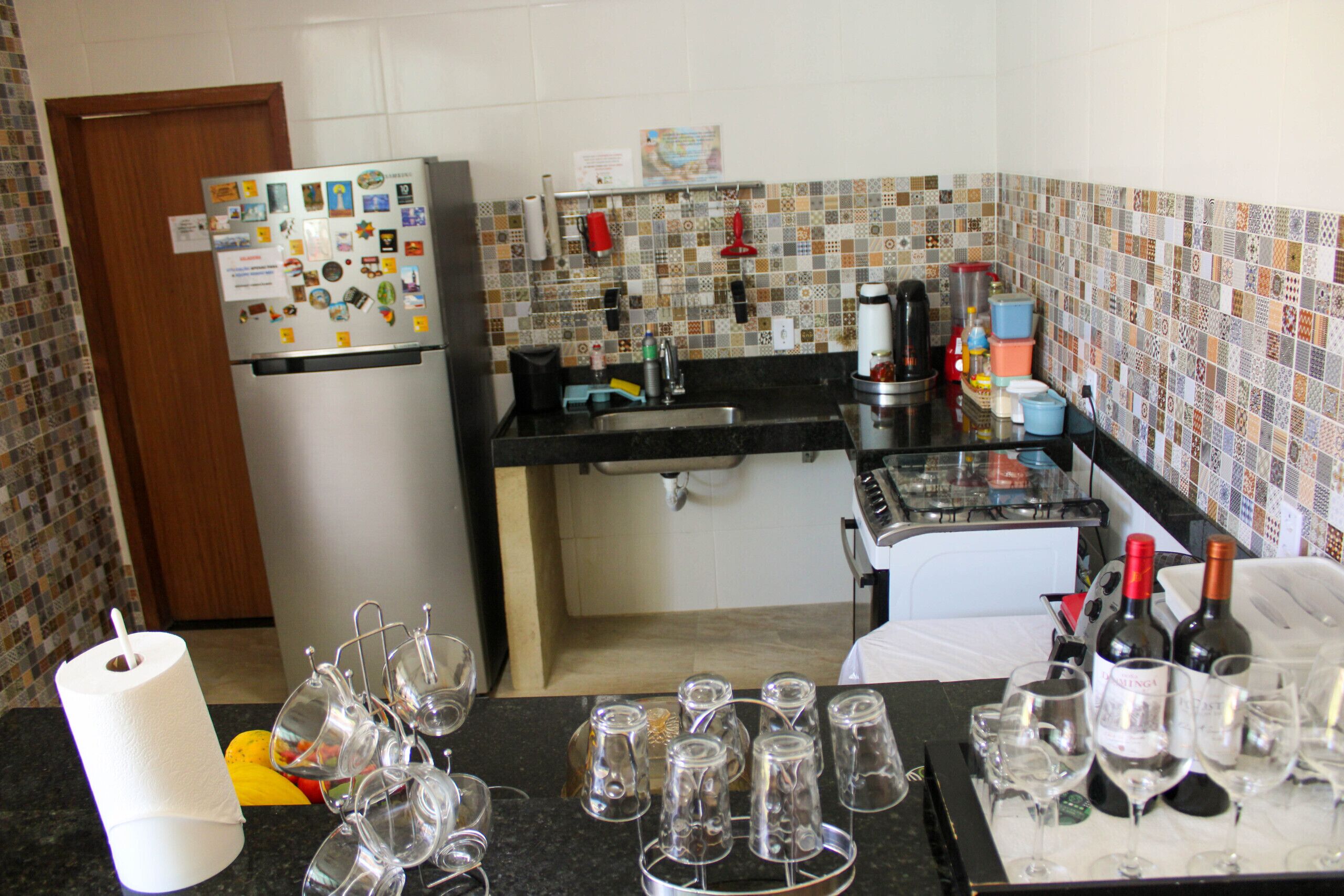 Cozinha com geladeira, cafeteira e garrafas de vinho.