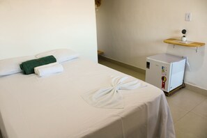 A hotel room with a bed, a small refrigerator, and a shelf with a plant.