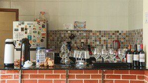 A kitchen counter with various items including a refrigerator, wine bottles, and a tiled backsplash. - Pousada Sonho Meu em Itaúnas - Quadruple Suite - QQP (Itaúnas)