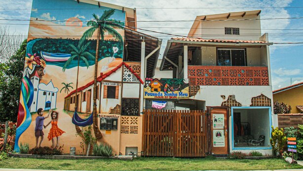 A building with a mural, a sign for 'Pousada Sonho Meu,' and a gated entrance. - Pousada Sonho Meu em Itaúnas - Quadruple Suite - QQP (Itaúnas)