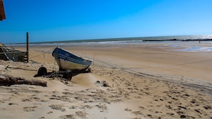 A beach with a boat, sandy shore, and clear sky. - Pousada Sonho Meu em Itaúnas - Quadruple Suite - QQP (Itaúnas)