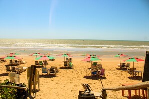 A beach with rows of sun loungers and umbrellas, a signboard, and a view of the ocean.