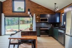 Una cocina moderna con paredes de madera, un comedor con mesa y sillas, y vista a un jardín.