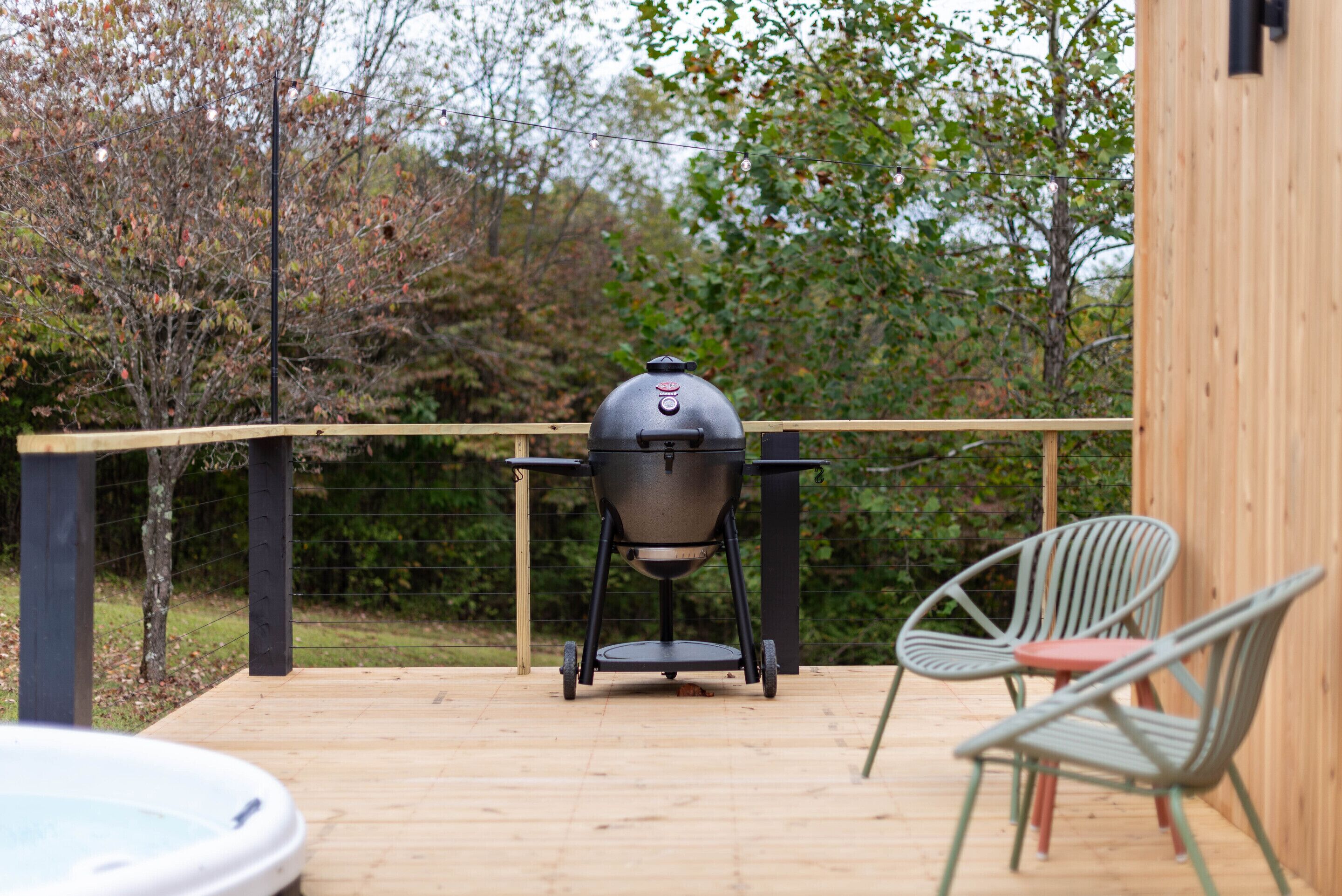 Une terrasse en bois équipée d’un barbecue, de deux chaises et d’un jacuzzi.