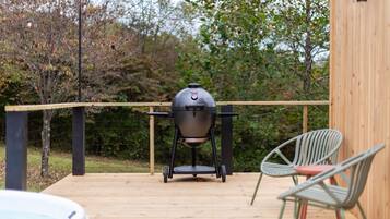 Une terrasse en bois équipée d’un barbecue, de deux chaises et d’un jacuzzi.