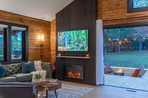 Ein gemütliches Wohnzimmer mit Kamin, einem an der Wand befestigten Fernseher und Blick ins Freie.