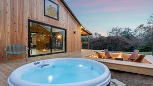 Ett trähus med en bubbelpool, utomhusmöbler och en eldstad.
