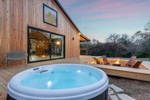 Una cabaña de madera con hidromasaje, mobiliario exterior y una fogata.