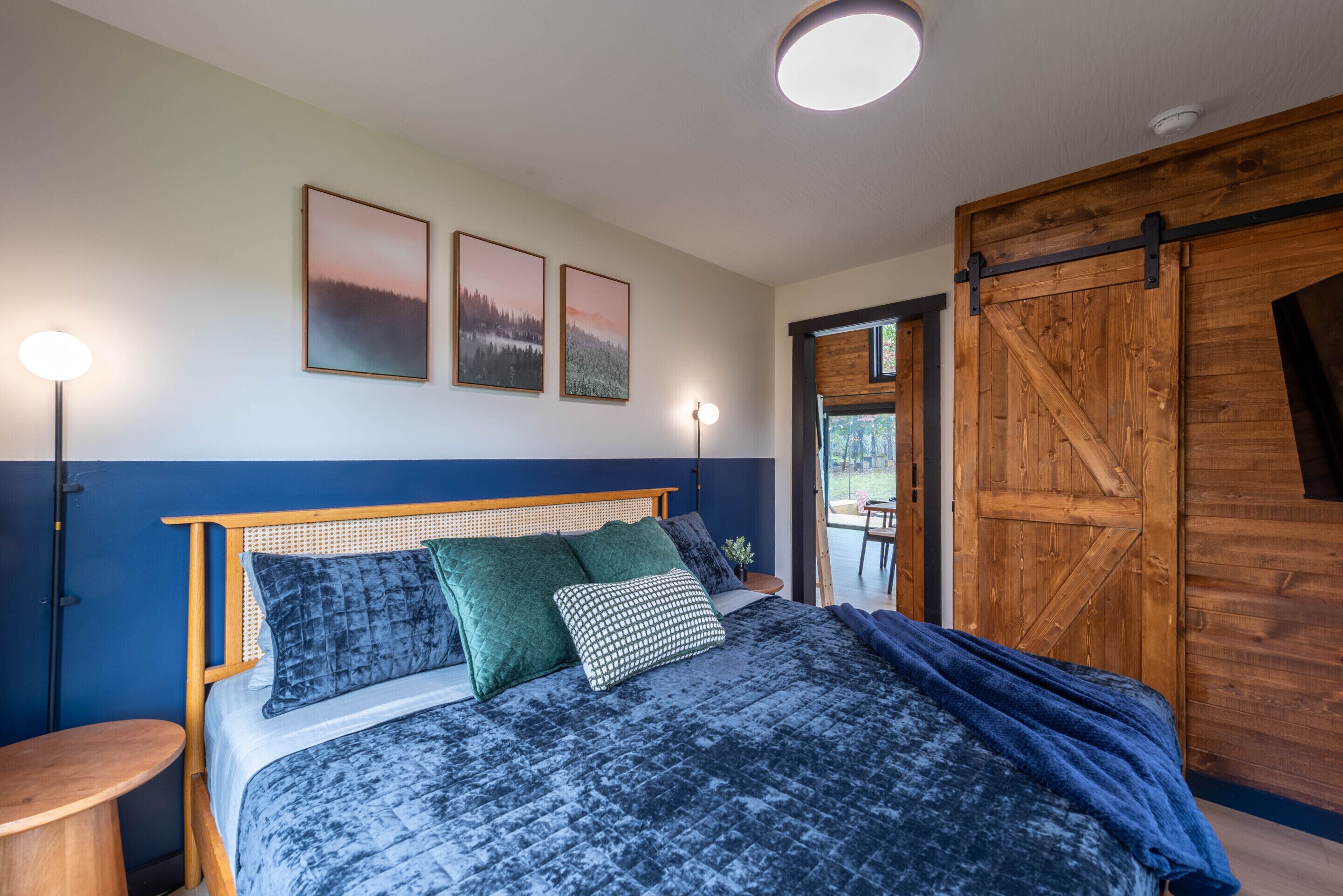 Ein Schlafzimmer mit Bett, Kissen, einem Nachttisch, einer Wandlampe und einer Holztür.