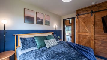 Ein Schlafzimmer mit Bett, Kissen, einem Nachttisch, einer Wandlampe und einer Holztür.
