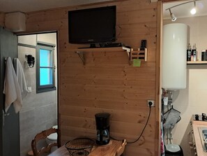 Ein Zimmer mit Holzwandverkleidung, einem Fernseher, einer Kaffeemaschine, einem Fön und einem Waschbecken mit Spiegel.