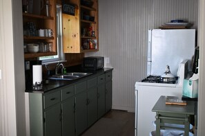 Eine Küche mit grünen Schränken, einem weißen Kühlschrank, einem Herd und einer Mikrowelle.