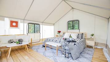 Een tentaccomodatie met een bed, zithoek en ramen.