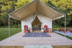 A tented accommodation with a wooden deck, two red Adirondack chairs, a picnic table, and a bed with pillows. - Summer Escape: Hike & Stargaze near Roaring River in Cassville, MO (Cassville)