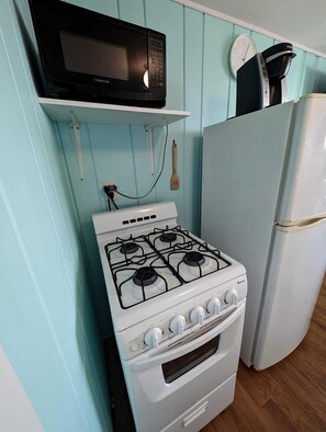 A kitchen with a gas stove, a microwave, a refrigerator, and a clock on the wall. - Romantic Beachfront Escape for Two in North Truro, Massachusetts (North Truro)