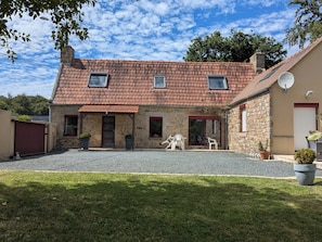 Ein Haus aus Stein mit Ziegeldach, einem Schotterweg und einer kleinen Terrasse mit Sitzgelegenheiten.