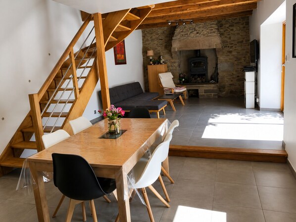 Ein modernes Interieur mit einer Holztreppe, einem Essbereich mit Tisch und Stühlen, einem Steinkamin und einem Fernseher.
