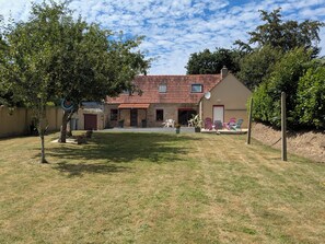 Ein Haus mit rotem Ziegeldach, Steinwänden, einer Veranda und Sitzgelegenheiten im Freien.