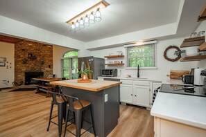 A modern kitchen with a central island, white cabinetry, a stone accent wall, and a built-in microwave. - Quaint Retreat w/ Fire Pit & Hot Tub! (McHenry)