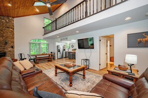 A spacious living room with a leather sofa, a wooden coffee table, and a staircase leading to an upper level. - Quaint Retreat w/ Fire Pit & Hot Tub! (McHenry)