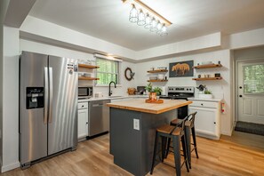 Eine moderne Küche mit einem Edelstahl-Kühlschrank, einer Holz-Kochinsel, Barhocker und integrierten Geräten.